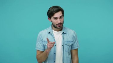 Yapma! Yapma! Kot pantolonlu genç adam hata uyarısı yapıyor. Uyarıcı parmak hareketi yapıyor. Onaylamıyor. Mavi arka planda kapalı stüdyo çekimleri
