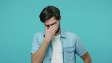 Kotlu tişörtlü mutsuz, dramatik sakallı adam ağlıyor ve gözyaşlarını siliyor, yenilgiyi yaşıyor, yalnızlık ve kederi içinde çaresiz hissediyor. Stüdyo çekimi mavi arkaplanda izole edildi