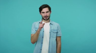 Senden nefret ediyorum! Kotlu tişörtlü sakallı adam kamerayı işaret ediyor ve baş parmaklarını aşağı gösteriyor. Seçimden memnun değil gibi görünüyor. Onaylamıyor işareti yapıyor. Mavi arka planda kapalı stüdyo çekimleri