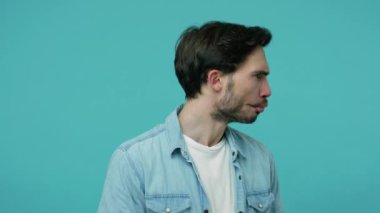 Kotlu tişörtlü komik sakallı adam etrafta dolanıp dudak bükmüş dudaklarıyla balık suratı yapıyor, kaşlarını çatıyor ve esprili, ihtiyatlı, şüpheli bir ifadeyle bakıyor. Mavi arka planda kapalı stüdyo çekimleri