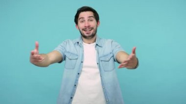 Kendimi seviyorum! Kot pantolonlu komik sakallı adam kendini kucaklıyor ve zevkten gülümsüyor, kendini rahat ve dolu hissediyor, halinden memnun. Mavi arka planda kapalı stüdyo çekimleri