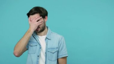Utangaç, şaşkın, kot gömlekli, elleri gözleri kapayan, parmaklarının arasından bakan utangaç ve utanç verici sırları merak eden, izlemeye korkan bir adam. Mavi arka planda kapalı stüdyo çekimleri