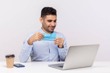Hijyenik maske tutan ve dizüstü bilgisayardan tıbbi ipuçları izleyen pozitif işadamı, bulaşıcı hastalık koronavirüsüne karşı koruyucu filtre kullanan ofis çalışanı, 2019-nCoV, grip salgını. Stüdyo çekimi izole