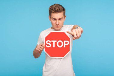 Kırmızı tişörtlü, elinde dur işareti olan ve kamerayı işaret eden genç ciddi bir adamın portresi, olumsuz bir ifadeyle, içki yasağı sembolüyle bakıyor. Mavi arka planda kapalı stüdyo çekimleri