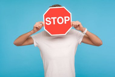 Beyaz tişörtlü kimliği belirsiz bir adamın portresi dur işareti ile kaplı, elinde kırmızı trafik işareti olan, yasaklama uyarısı konulu bir tabela. Mavi arka planda kapalı stüdyo çekimleri
