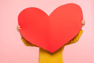 Unrecognizable person hiding behind large red paper heart, holding symbol of love affection fondness, anonymous charity and care concept, cardiac health. indoor studio shot isolated on pink background clipart