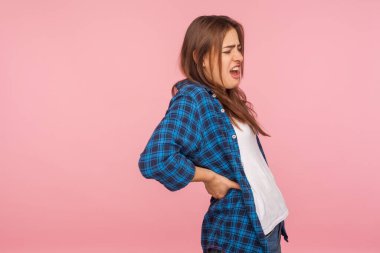 Sırt ağrısı. Kareli tişörtlü, sırt ağrısı çeken, böbrek iltihabı olan, yerleşik yaşam tarzından dolayı ağrılı kas spazmları geçiren bir kız portresi. Pembe arka planda kapalı stüdyo çekimleri