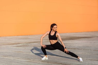 Dar spor giysili, siyah pantolonlu, üstü açık havada antrenman yapan daha iyi esneklik için esneme egzersizleri yapan, vücudunun alt kısımlarını çalıştıran zayıf ve güzel bir kadın. Sağlık konsepti, spor aktivitesi