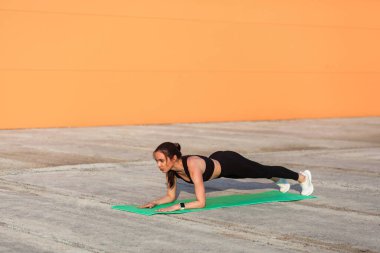 Dar spor giysili zayıf esmer kadın, siyah pantolon ve üst, yoga yapıyor, Ardha Phalakasana 'nın düşük tahta duruşunda duruyor, kaslarını ve gücünü çalıştırıyor. Sağlık hizmetleri, dışarıda spor faaliyetleri