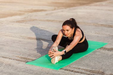 Sıkı spor giyimli, siyah pantolonlu, üstsüz, yoga yapan, dizinden dizine kadar poz veren ayak parmaklarına dokunan, bacak ve sırt kaslarını esneten pozitif atletik bir kadın. Sağlık hizmetleri, dışarıda spor faaliyetleri