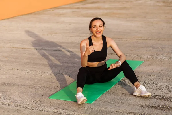 Delighted Athletic Girl Black Pants Top Smiling Showing Thumbs Sitting — Stock Photo, Image