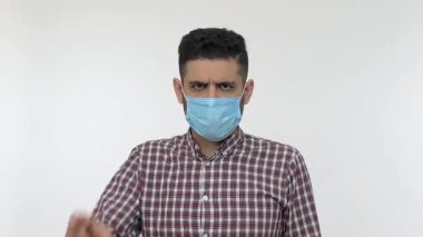 Hijyenik maskeli bir adam kameraya işaret ediyor ve onaylamıyor. Tavsiye veriyor. Bulaşıcı koronavirüs hastalığı, viral enfeksiyon ve grip salgınına karşı yüz koruması takın diyor. izole