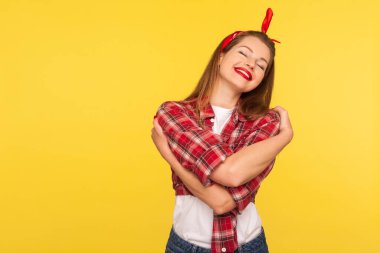 Kendimi seviyorum! Parlak makyajlı, kareli gömlekli, kendini kucaklayan, zevkten gülümseyen, yalnız başına mutlu bir kızın portresi. 50 'li yılların modası, stüdyo çekimi, izole edilmiş.