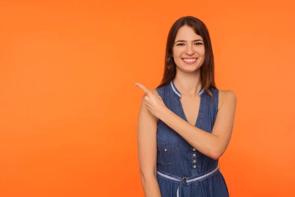 Kijk Reclamegebied Vrolijke Vrolijke Brunette Vrouw Spijkerjurk Glimlachend Wijzend Vinger — Stockfoto