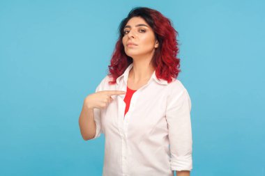 I'm the best! Portrait of egoistic hipster woman with fancy red hair pointing herself, looking with arrogance, feeling confident and self-important. indoor studio shot isolated on blue background clipart