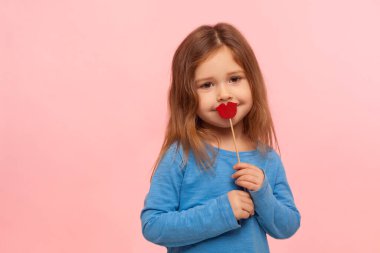 Güzel, tatlı esmer küçük kızın portresi. Ağzı kırmızı kağıt dudaklarla ya da kalp şekliyle kaplayan. Kameraya, modaya ve güzellik anlayışına nazikçe bakan. Pembe arka planda kapalı stüdyo çekimleri