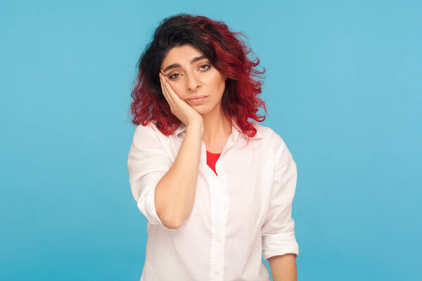 Portrait of fatigued hipster woman with fancy red hair listening to boring story with dull indifferent face, dismal look, depressing view of life. indoor studio shot isolated on blue background