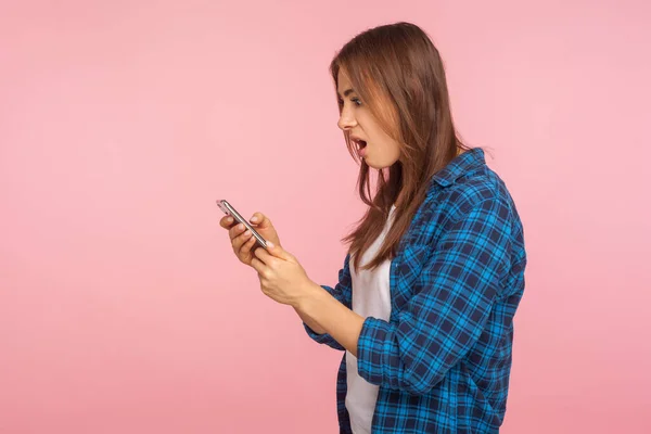 モバイル接続 ショックを受けたシャツを着たショックを受けた少女のサイドビューは 携帯電話を使用してソーシャルネットワーク上でチャット信じられないほどのニュースを見て驚いた ピンクの背景に隔離されたスタジオショット — ストック写真