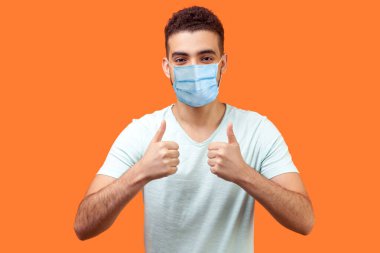 Gibi! İyimser yakışıklı bir adamın portresi, beyaz tişörtlü, başparmak hareketi yapan, gülümseyen, iyi iş çıkaran, iyimser bir adam. Turuncu arka planda kapalı stüdyo çekimleri