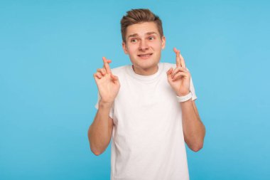 Kazanma umuduyla. Sıradan beyaz tişörtlü bir adamın portresi şans getirmesi ve umutla bakması, başarı dilemesi. Mavi arka planda kapalı stüdyo çekimleri