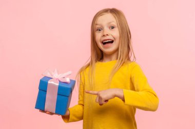 Portrait of delighted amazed little girl pointing gift box, boasting present and looking with astonishment to camera, shocked by birthday surprise. indoor studio shot isolated on pink background clipart