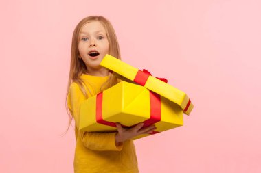 Charming child surprised by birthday present. Portrait of cute little girl opening gift box and keeping mouth open in amazement, shocked expression. indoor studio shot isolated on pink background clipart