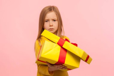Funny cute child unhappy with bad birthday present. Portrait of sad little girl opening gift box and looking at camera with dissatisfied expression. indoor studio shot isolated on pink background clipart