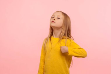 Ben buyum! Kendini beğenmiş, kendine güvenen, gururla bakan, zaferle övünen ünlü ve başarılı bir anaokulu kızının portresi. Pembe arka planda kapalı stüdyo çekimleri