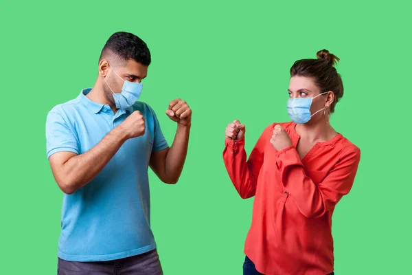 戦いましょう 外科用医療マスクを持つカップルの肖像画が一緒に立って 拳をきれいに保ち 戦うためにお互いを見て 冗談を言います 緑の背景室内に隔離され — ストック写真