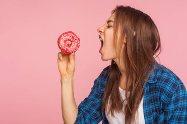Deli gibi aç suratlı, donut yemek isteyen, tatlı çörek yemeyi hayal eden, şekerli şekerleme yeme arzusuyla mücadele eden bir kızın profili. Pembe arka planda kapalı stüdyo çekimleri