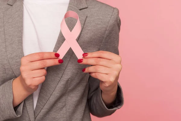 Closeup of business person in elegant suit jacket holding pink ribbon, warning of breast cancer risk and society awareness, female health care, medical insurance. indoor studio shot, pink background