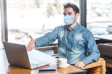 Hoşgeldiniz! Tıbbi maskeli tatmin olmuş bir iş adamının portresi. Bir işçiyi web kamerasından selamlıyor ve gülümseyerek el sıkışma hareketi yapıyor. kapalı çalışma ve sağlık hizmeti kavramı.