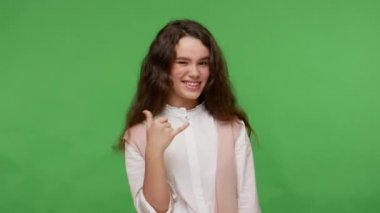 Ara beni! Beyaz tişörtlü güzel esmer kız telefon işareti yapıyor ve kamerayı işaret ediyor, seninle iletişim kurmayı bekliyor, telefonla iletişim kuruyor. Yeşil arka planda izole edilmiş kapalı stüdyo çekimi