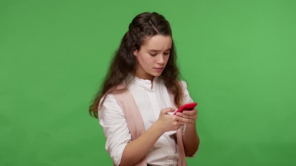 漂亮的少女黑发女孩会三思而后行 用智能手机打字 在网上与朋友聊天 在社交媒体上发帖 在绿色背景下隔离的室内拍摄 — 图库视频影像