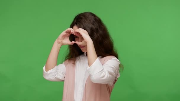 白いシャツの好奇心10代のブルネットの少女は 双眼鏡の手のジェスチャーを通して世界を観察し 距離を見て 気配りのある探究的なビューで周りを見回す 屋内スタジオで撮影した緑の背景 — ストック動画