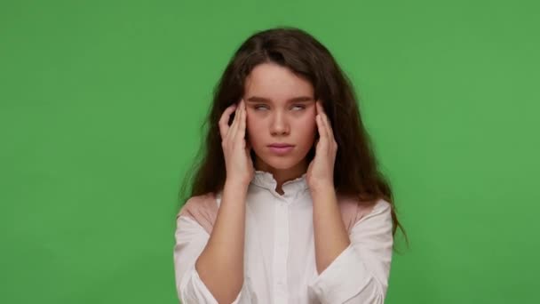白いシャツの病気の十代のブルネットの女の子は彼女の寺院をこすり 青年期の片頭痛 ストレスとうつ病 インフルエンザ熱を経験している スタジオは緑の背景に隔離され — ストック動画