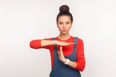 Ara vermem lazım! Tulumlu, kot pantolonlu, canı sıkkın bir kızın portresi. Mola verme hareketi yapıyor ve tatminsiz bir ifadeyle bakıyor. Beyaz arka planda izole edilmiş kapalı stüdyo çekimi