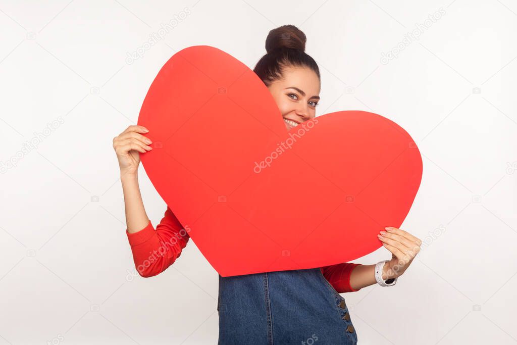 Be my Valentine! Portrait of playful charming happy girl hiding behind big red paper heart and smiling seductively to camera, expressing love, flirting. indoor studio shot isolated on white background