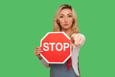 Yasaklandın, erişimin yok, gitmen yasak! Elinde sekizgen kırmızı trafik levhası tutan ve kamerayı işaret eden ciddi bir yetişkin kadının portresi. Yeşil arka planda izole edilmiş kapalı stüdyo çekimi