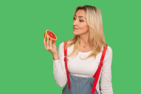 解毒食品 维生素的饮食 多愁善感的成年女子的画像 看着切片多汁的新鲜柚子 表情深沉 营养健康 在绿色背景下隔离的工作室拍摄 — 图库照片