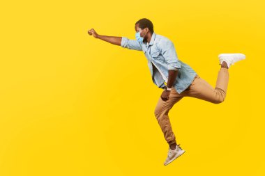 Tıbbi maskeli, havalı, yakışıklı bir adamın uzun bir portresi havada zıplayan ya da tek koluyla yüksekten uçan, Süpermen gibi hisseden. Sarı arka planda izole edilmiş kapalı stüdyo çekimi