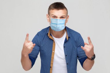 Cerrahi maske takmış, boynuzlu ve kameraya bakan sıradan bir genç portresi. Sağlık ve tıbbi konsept. Gri arka planda izole edilmiş kapalı stüdyo görüntüleri..