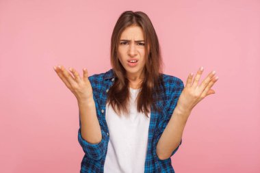 Sen ne istiyorsun? Kareli gömlekli bir kızın portresi sorgulama jesti ile kollarını kaldırıyor, sorunu anlamadığımı söylüyor, kızgın görünüyor. Pembe arka planda kapalı stüdyo çekimleri