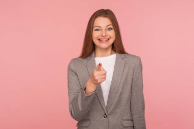 Hey sen! İş elbisesi içindeki mutlu, iyimser genç bir kadının portresi parmağını göstererek seçim yapıyor, mutlu görünüyor, şanslı kazananı gösteriyor. Stüdyo çekimi pembe arkaplanda izole edildi