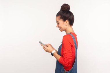 Çevrimiçi iletişim. Pozitif sosyal medya kullanıcısının yan görüntüsü, cep telefonuyla mesajlaşan mutlu kız ve gülümseyen, blog yazıları yazan, cep telefonuyla internette gezinen kız. Stüdyo beyaz arkaplan