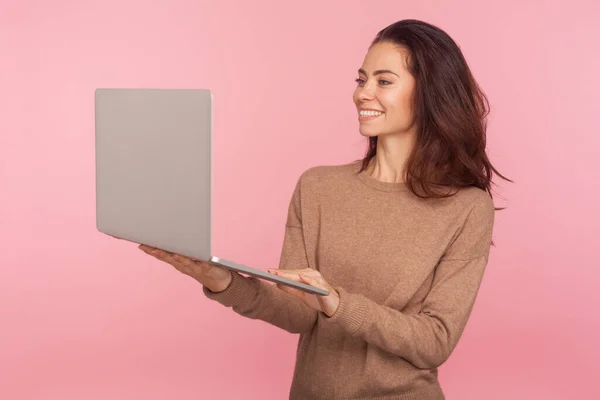 カジュアルなセーターを着た若い女性の肖像画 ビデオ通話で話している間にノートパソコンと笑顔を保持し オンライン会議を持っている コンピュータ上で働くフリーランス 屋内スタジオでの撮影は — ストック写真