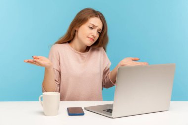 Bilmiyorum! Bilmiyorum! Şaşırmış bir kadın sorgulama jesti ile kollarını kaldırıyor ve laptop ekranına bakıyor, görüntülü konuşma yapıyor, merkez ofisten online konferans yapıyor. Kapalı alan stüdyo görüntüleri izole, mavi arkaplan