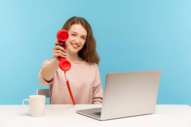 Pozitif çağrı merkezi operatörü, kadın sekreter iş yerinde oturuyor ve eski moda bir telefon ahizesini tutuyor, arkadaşça gülümsüyor, telefona cevap vermek istiyor. Mavi arka planda kapalı stüdyo çekimleri