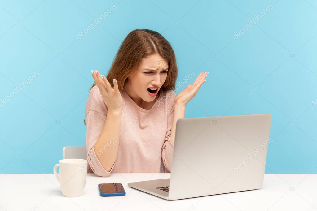 How could you? Irritated young woman employee raising hands in indignant gesture, asking why and looking at laptop screen, talking on video call. indoor studio shot isolated on blue background