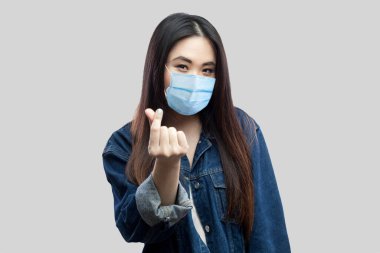 Sıradan mavi kot ceketli komik esmer Asyalı genç kadın portresi ayakta duruyor, para hareketi yapıyor ve kameraya bakıyor. Stüdyo çekimi, gri arkaplanda izole edilmiş..